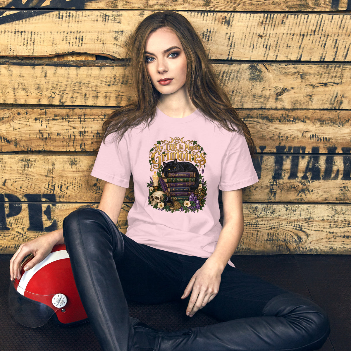 My TBR Is Mostly Grimoires dark academia design, a black cat guarding a stack of grimoires beside a skull, on a soft pink unisex t-shirt, front view