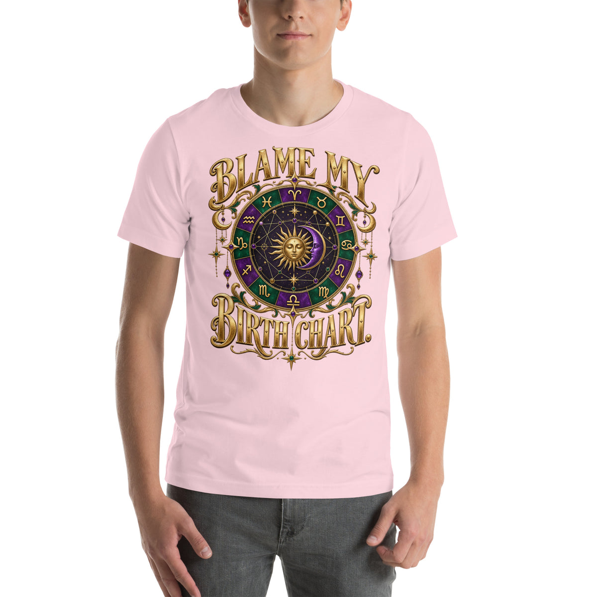 Blame My Birth Chart astrology design, a purple and green zodiac wheel with a gold sun face and crescent moon at its center, hung with gold ornaments, on a soft pink unisex t-shirt, front view