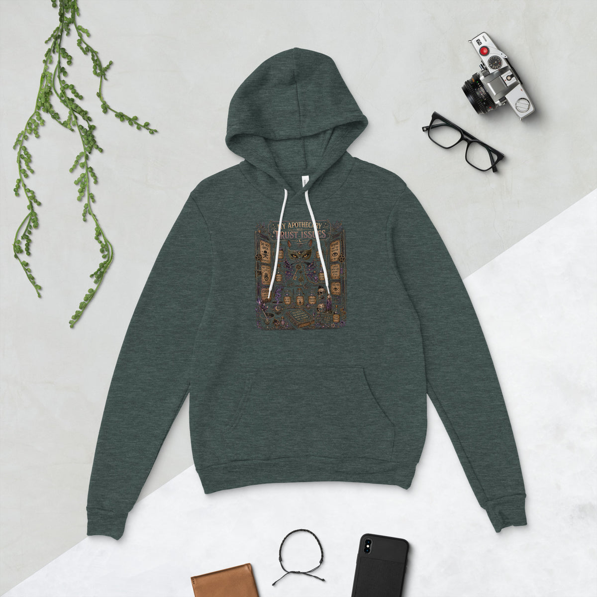 My Apothecary Has Trust Issues, a witchy black cat and a cabinet of potion bottles, on a heather forest unisex pullover hoodie, front view