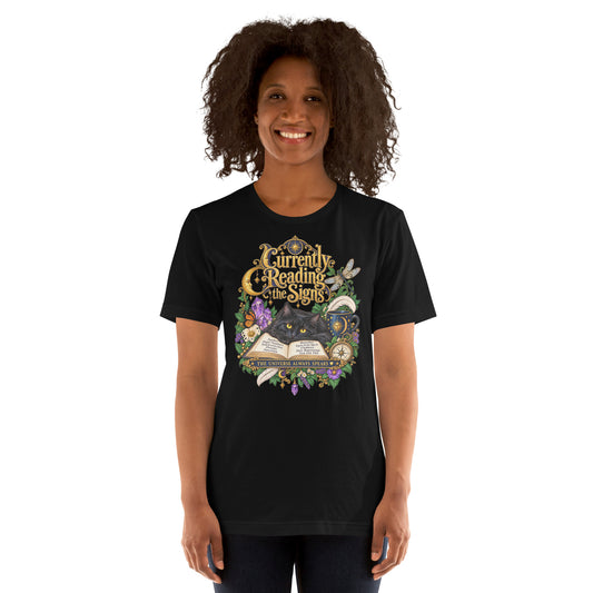 Currently Reading The Signs dark academia design, two black cats asleep over an open book beneath a crescent moon, on a black unisex t-shirt, front view