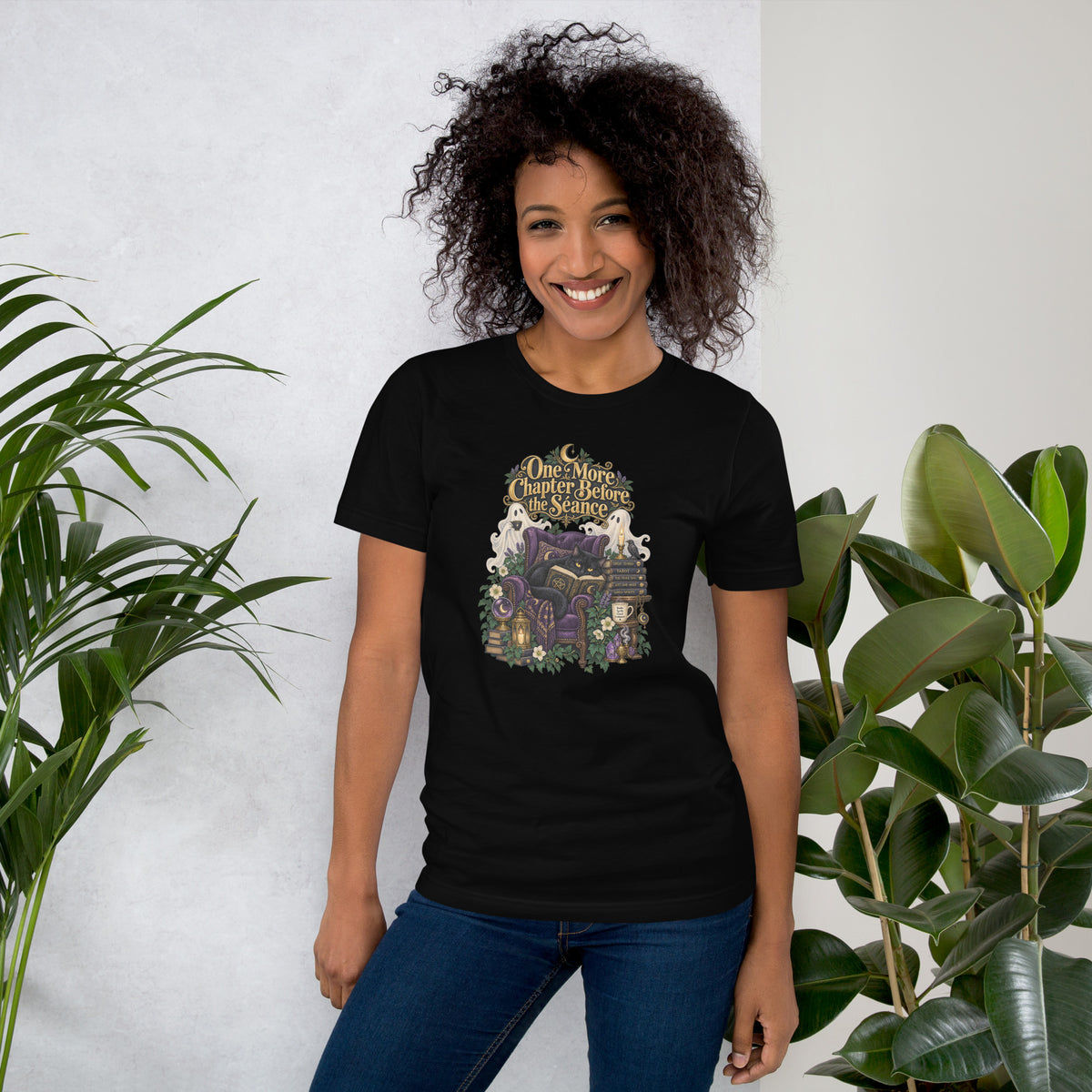 One More Chapter Before The Séance dark academia design, a black cat reading in a velvet armchair with two ghosts, on a black unisex t-shirt, front view