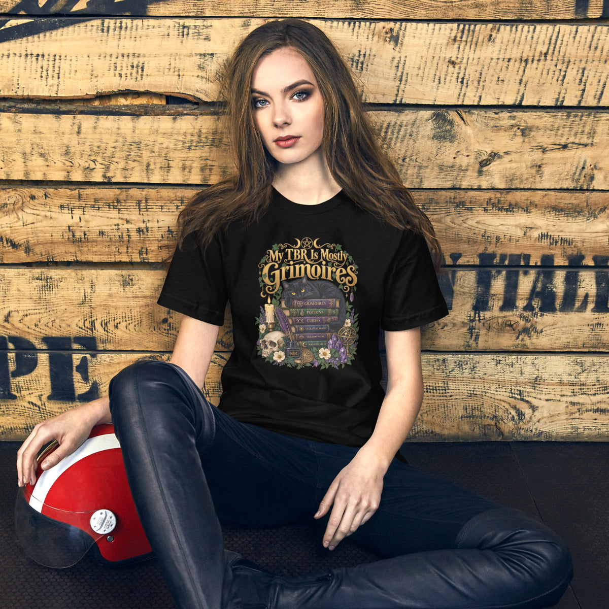 My TBR Is Mostly Grimoires dark academia design, a black cat guarding a stack of grimoires beside a skull, on a black unisex t-shirt, front view