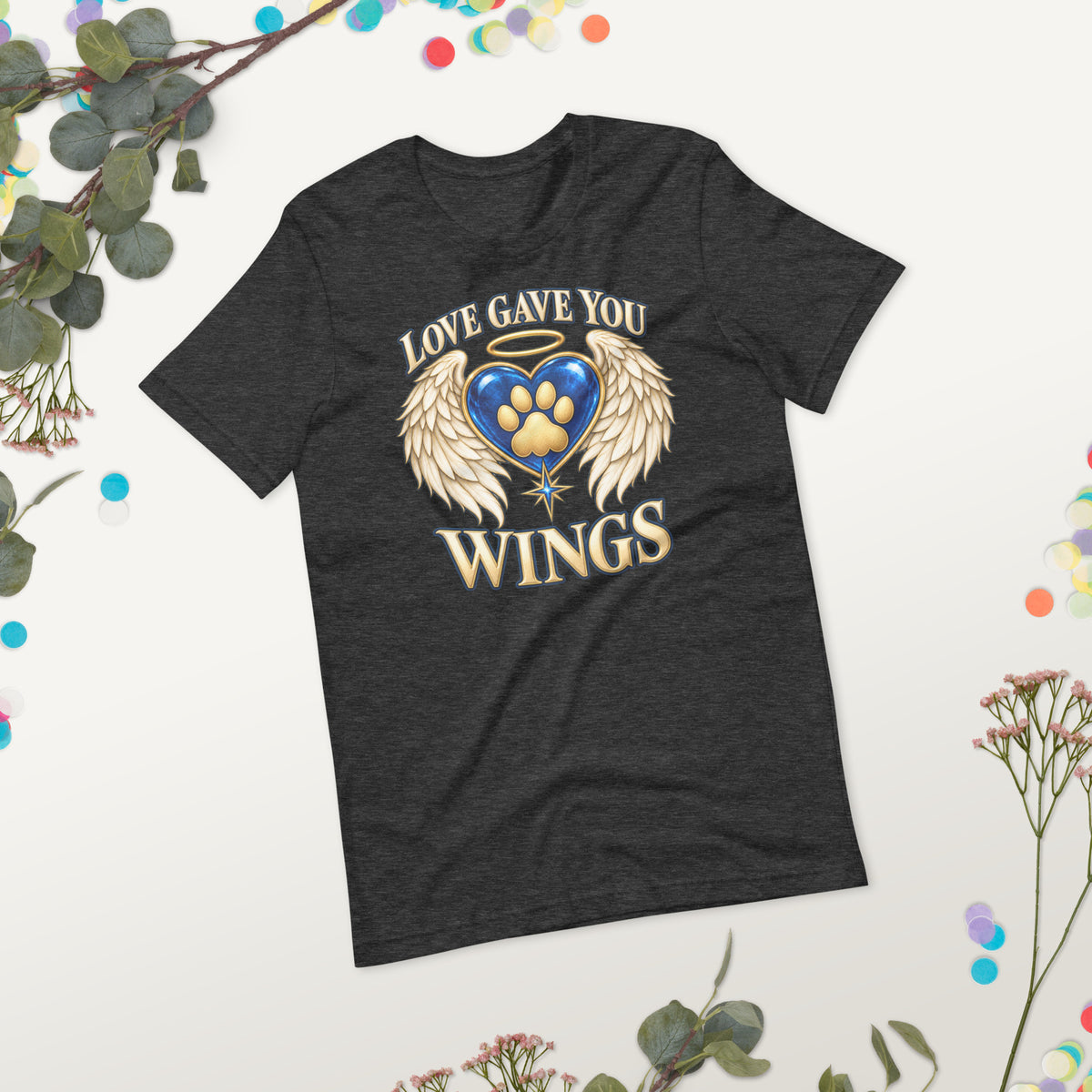 Love Gave You Wings design, a blue gem heart with a gold halo, cream angel wings and a gold cat paw print at its center, under gold lettering, on a dark grey heather unisex t-shirt, styled flat lay on a gray backdrop