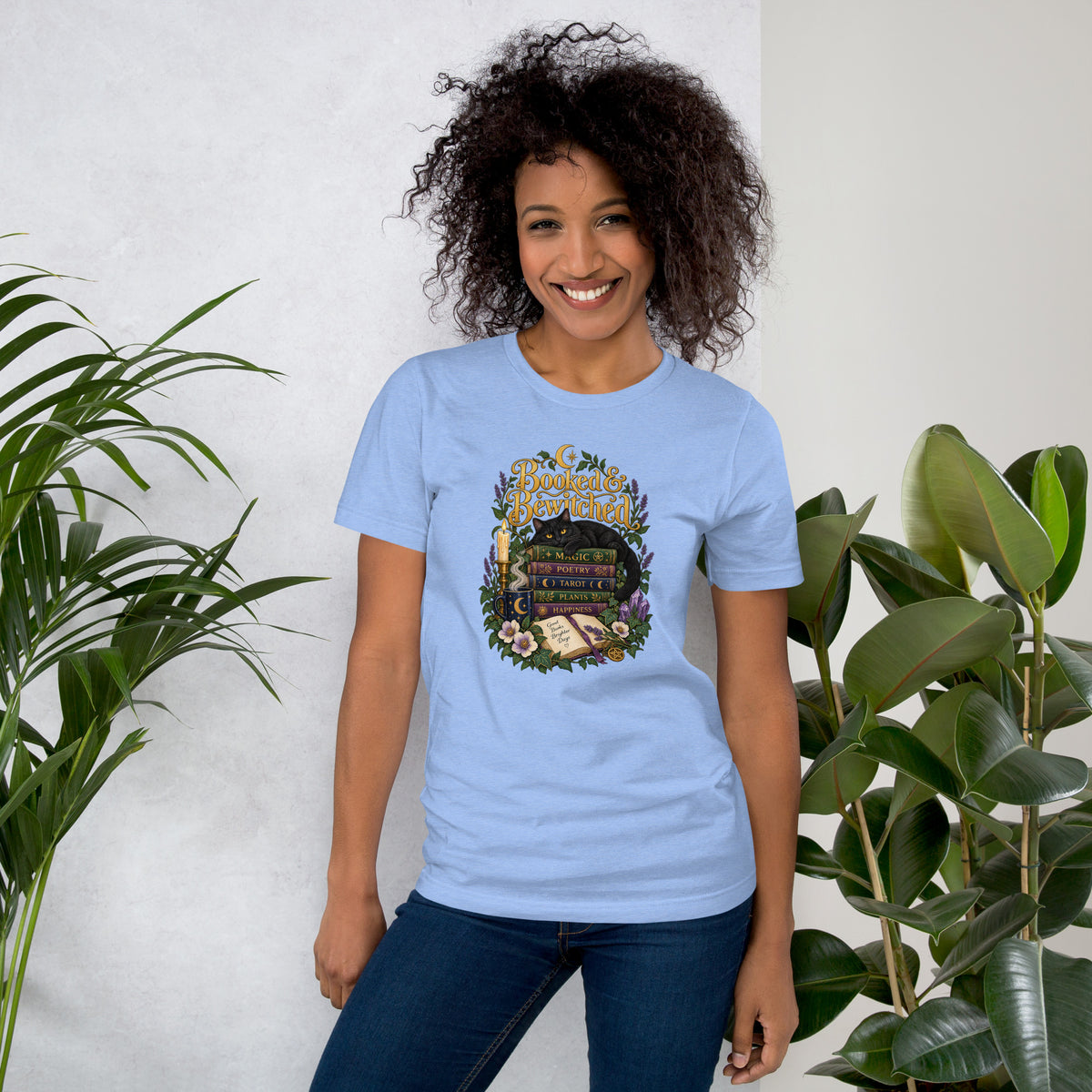 Booked and Bewitched dark academia design, a black cat asleep on a stack of spellbooks, on a heather carolina blue unisex t-shirt, front view