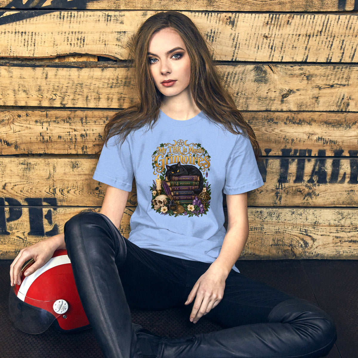 My TBR Is Mostly Grimoires dark academia design, a black cat guarding a stack of grimoires beside a skull, on a heather carolina blue unisex t-shirt, front view