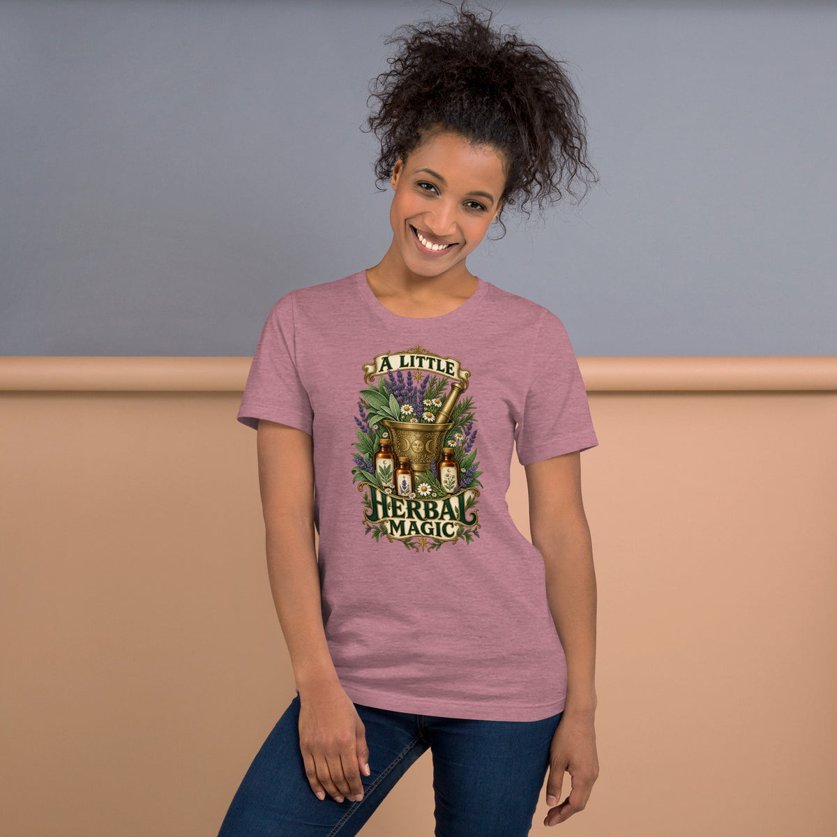 A Little Herbal Magic design, a gold mortar and pestle bearing a moon face, filled with lavender and chamomile and flanked by amber apothecary bottles, with the words on gold banners, on a heather orchid unisex t-shirt, front view