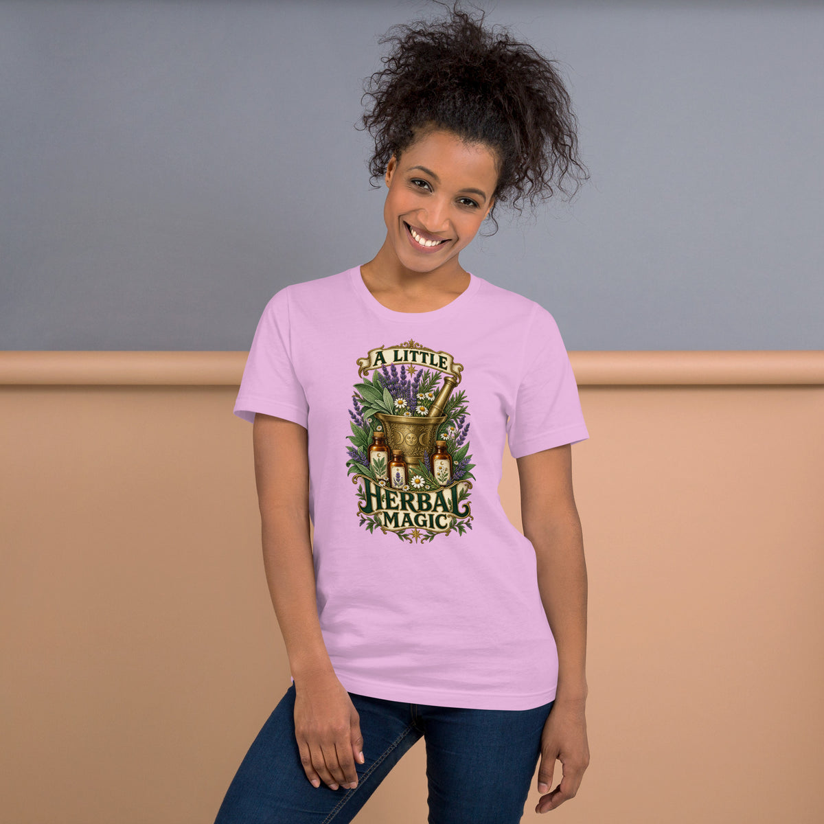 A Little Herbal Magic design, a gold mortar and pestle bearing a moon face, filled with lavender and chamomile and flanked by amber apothecary bottles, with the words on gold banners, on a lilac unisex t-shirt, front view