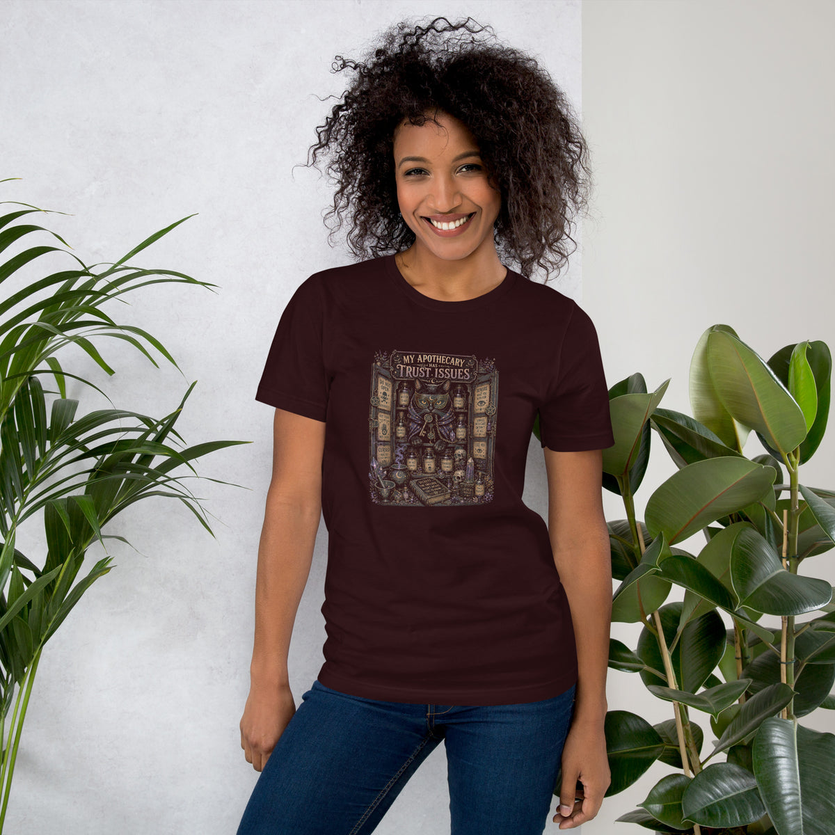 My Apothecary Has Trust Issues, a witchy black cat and a cabinet of potion bottles, on an oxblood black unisex t-shirt, front view