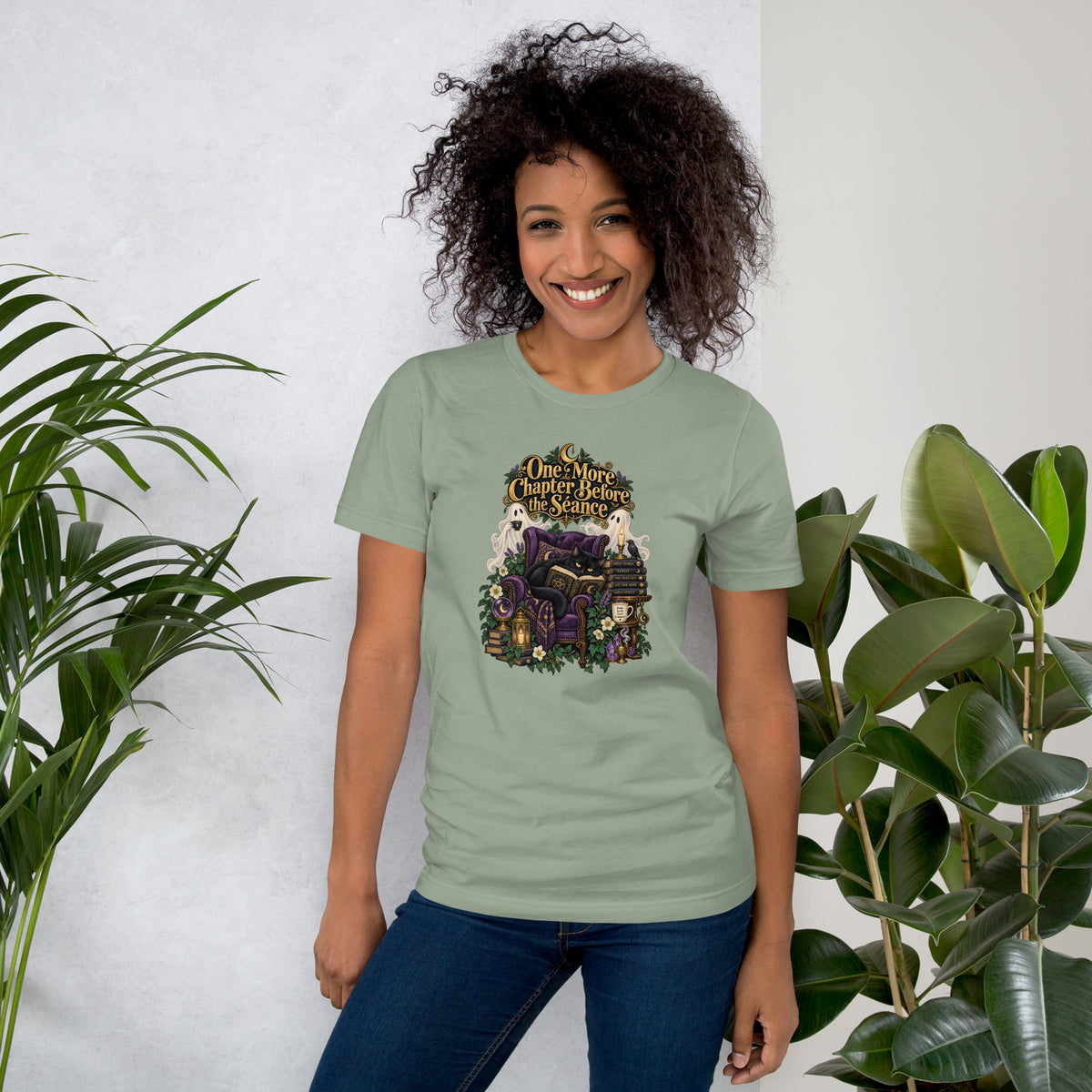 One More Chapter Before The Séance dark academia design, a black cat reading in a velvet armchair with two ghosts, on a sage unisex t-shirt, front view