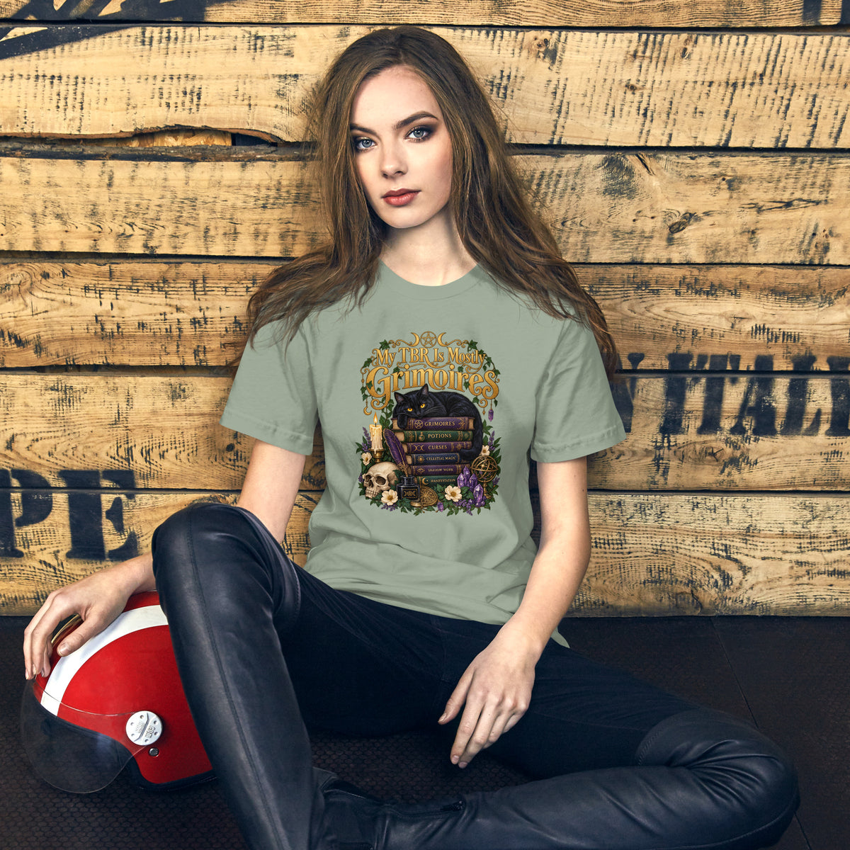 My TBR Is Mostly Grimoires dark academia design, a black cat guarding a stack of grimoires beside a skull, on a sage unisex t-shirt, front view