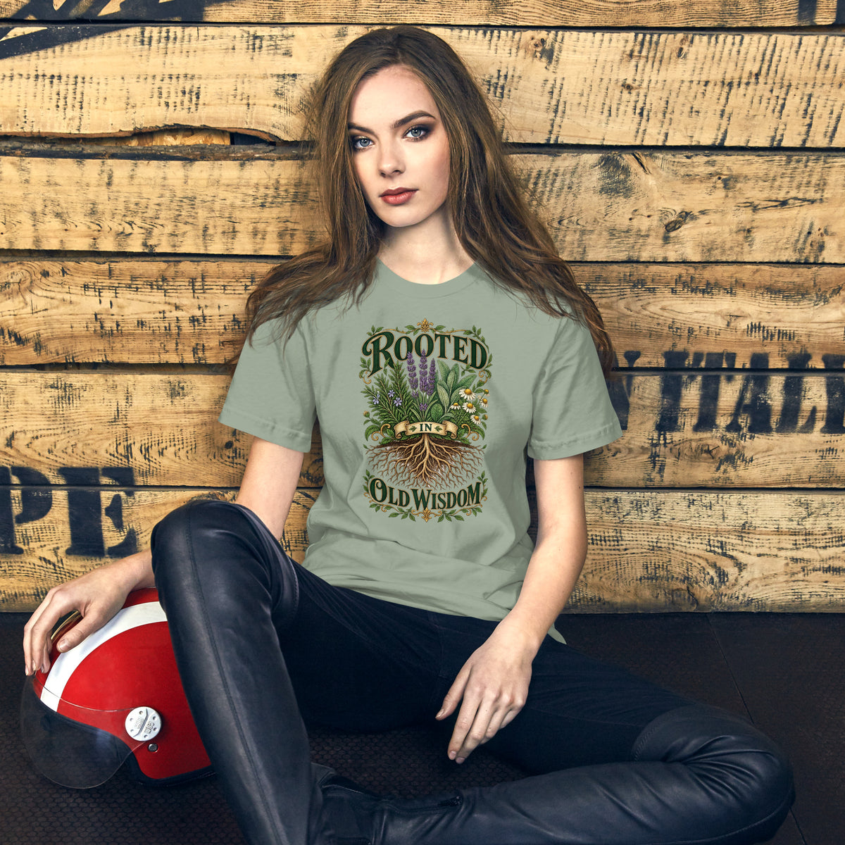Rooted in Old Wisdom design, lavender, sage and chamomile growing above an exposed root system, with the words in dark green and gold inside a gold scrollwork border, on a sage unisex t-shirt, front view