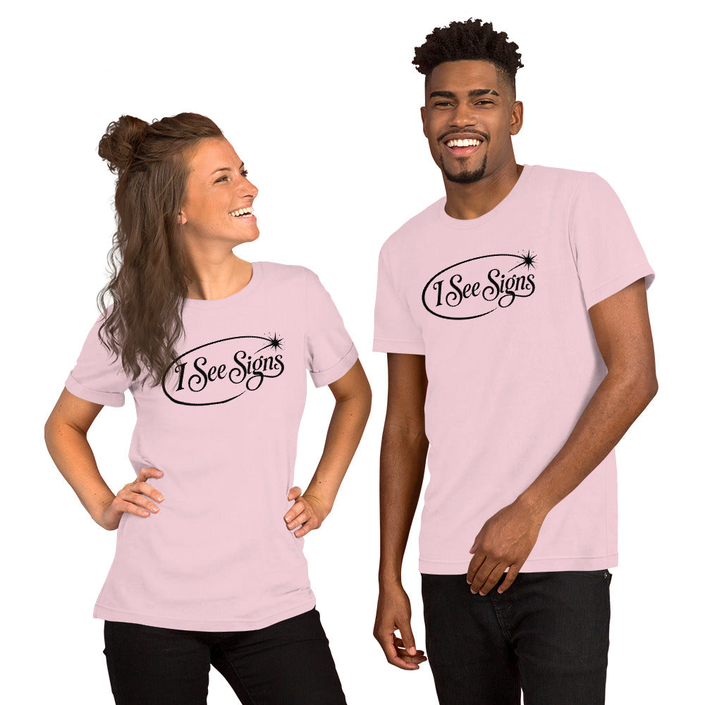 I See Signs design, the words set in black script inside a thin oval with a four-pointed star, on a soft pink unisex t-shirt, front view