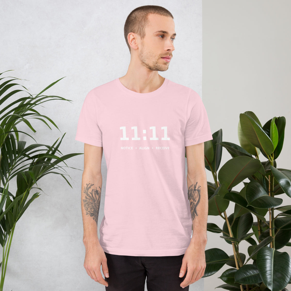 11:11 angel number design, the number set in plain white type above Notice, Align, Receive, on a soft pink unisex t-shirt, front view