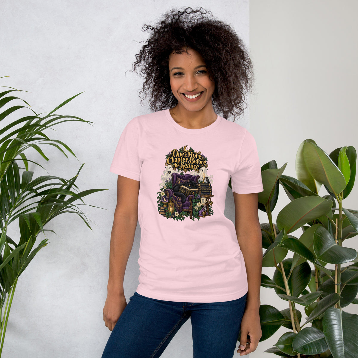 One More Chapter Before The Séance dark academia design, a black cat reading in a velvet armchair with two ghosts, on a soft pink unisex t-shirt, front view
