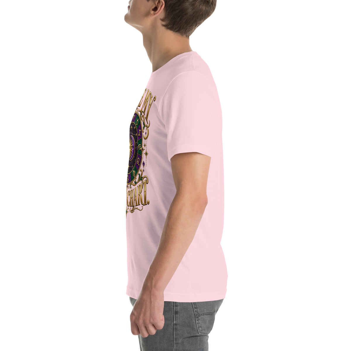 Blame My Birth Chart astrology design, a purple and green zodiac wheel with a gold sun face and crescent moon at its center, hung with gold ornaments, on a soft pink unisex t-shirt, left side view