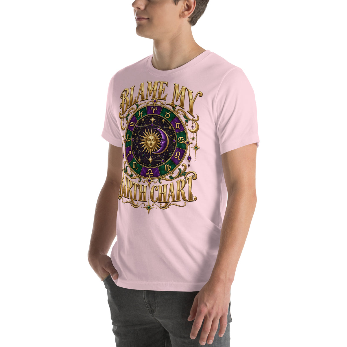 Blame My Birth Chart astrology design, a purple and green zodiac wheel with a gold sun face and crescent moon at its center, hung with gold ornaments, on a soft pink unisex t-shirt, angled left front view
