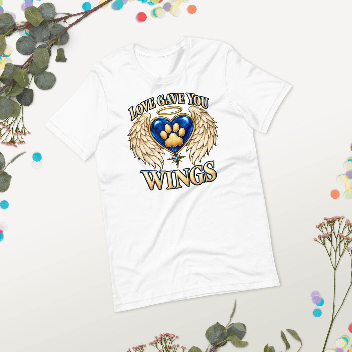 Love Gave You Wings design, a blue gem heart with a gold halo, cream angel wings and a gold cat paw print at its center, under gold lettering, on a white unisex t-shirt, styled flat lay on a gray backdrop