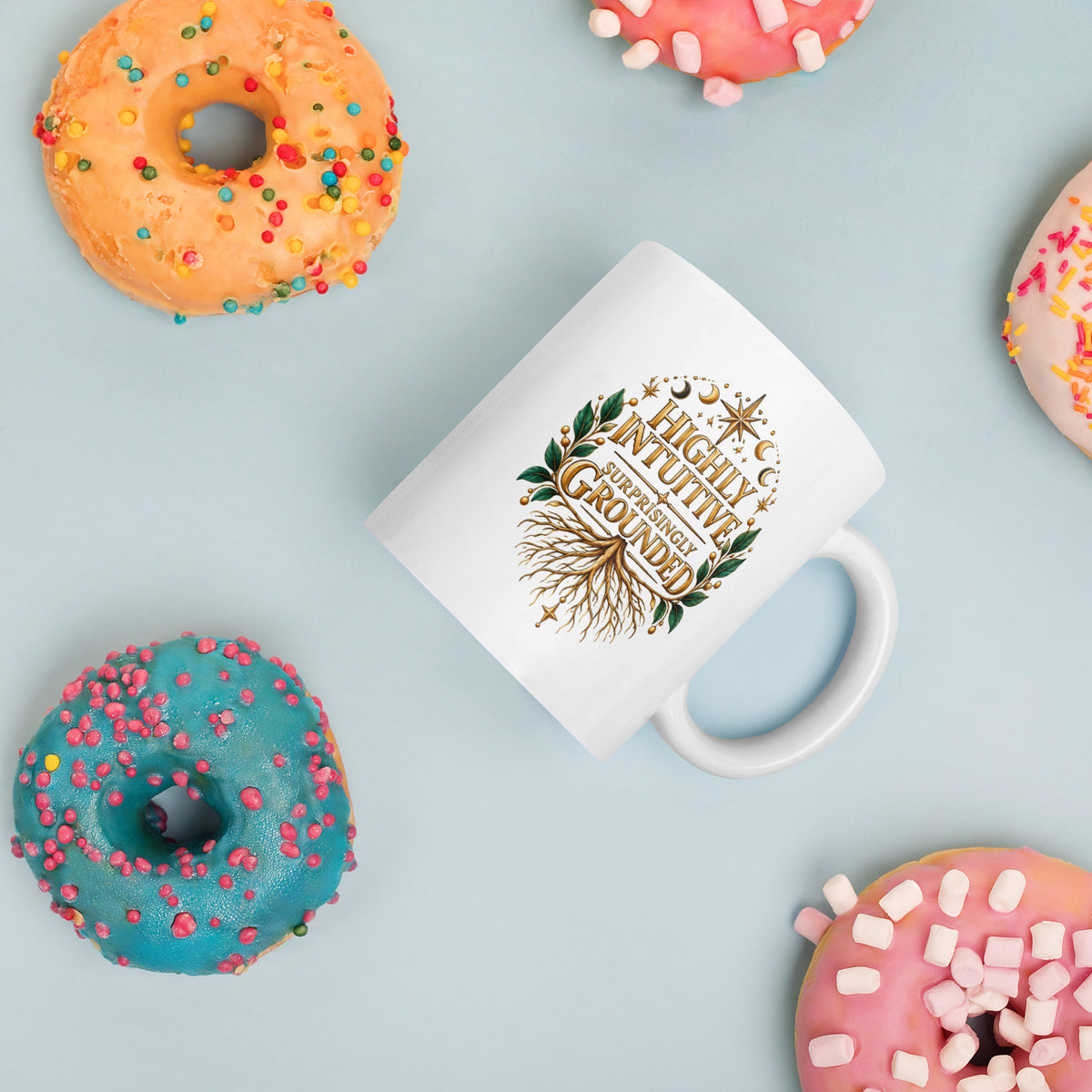 Highly Intuitive, Surprisingly Grounded design, moon phases above and roots below, on a white glossy mug, 11 oz, styled with donuts