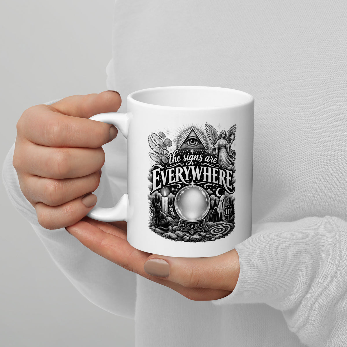 The Signs Are Everywhere design, an all-seeing eye, an angel, a crystal ball, a black cat and a 111 road sign, in black and white line art, on a white glossy mug, 11 oz, handle on the left