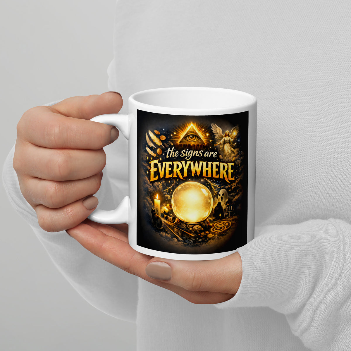 The Signs Are Everywhere design, an all-seeing eye, an angel, a glowing crystal ball, a ghost and a 111 road sign, in gold on black, on a white glossy mug, 11 oz, handle on the left