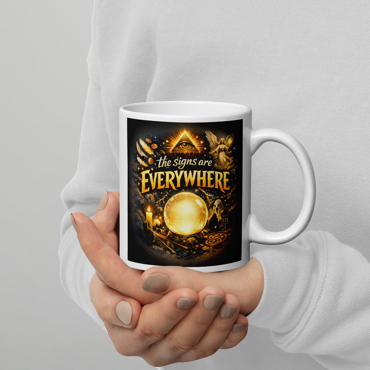 The Signs Are Everywhere design, an all-seeing eye, an angel, a glowing crystal ball, a ghost and a 111 road sign, in gold on black, on a white glossy mug, 11 oz, handle on the right