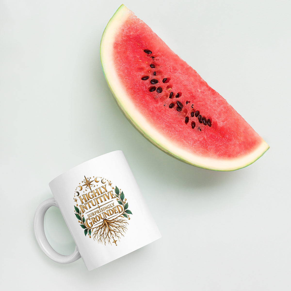 Highly Intuitive, Surprisingly Grounded design, moon phases above and roots below, on a white glossy mug, 11 oz, styled with watermelon