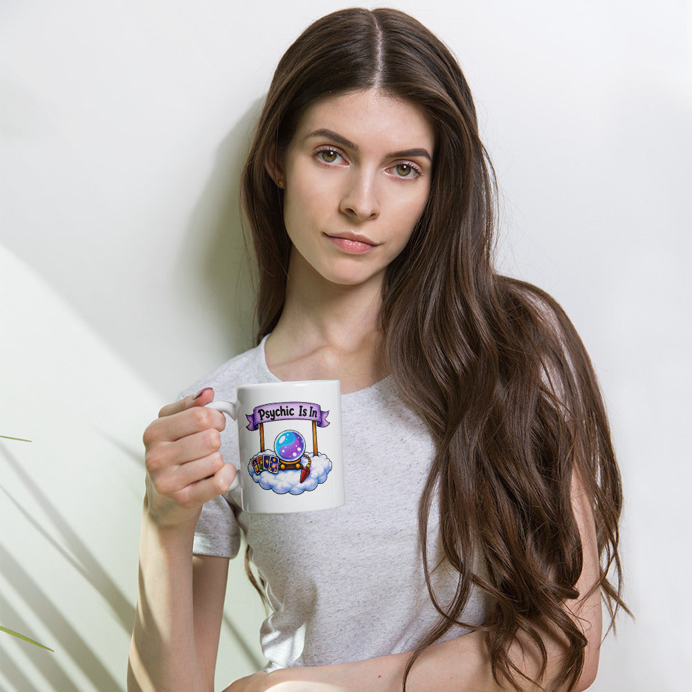 Psychic Is In design, playful floating clouds beneath a banner that reads Psychic Is Open for Business, on a white glossy mug, 11 oz, held by a model