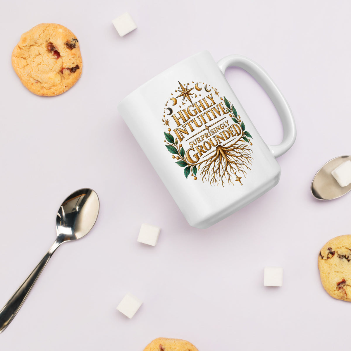 Highly Intuitive, Surprisingly Grounded design, moon phases above and roots below, on a white glossy mug, 15 oz, styled with cookies