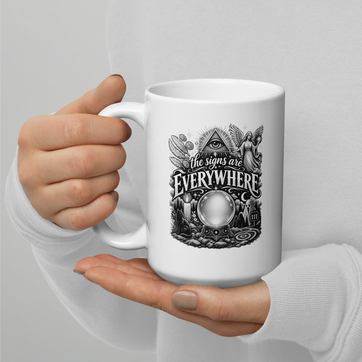 The Signs Are Everywhere design, an all-seeing eye, an angel, a crystal ball, a black cat and a 111 road sign, in black and white line art, on a white glossy mug, 15 oz, handle on the left