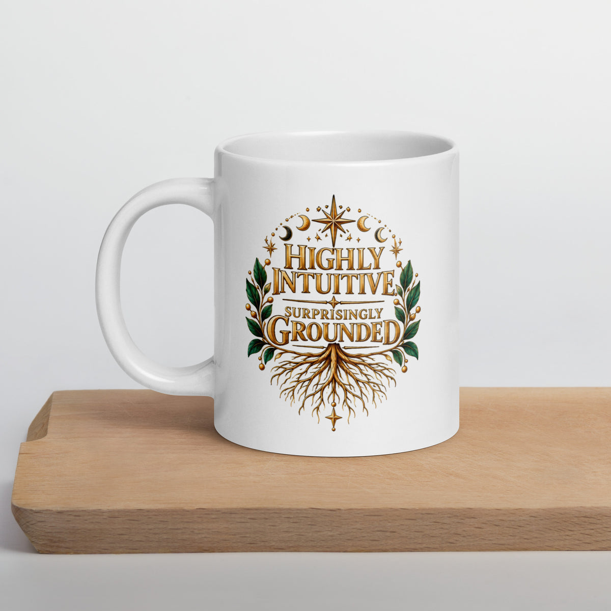 Highly Intuitive, Surprisingly Grounded design, moon phases above and roots below, on a white glossy mug, 20 oz, set on a wooden cutting board