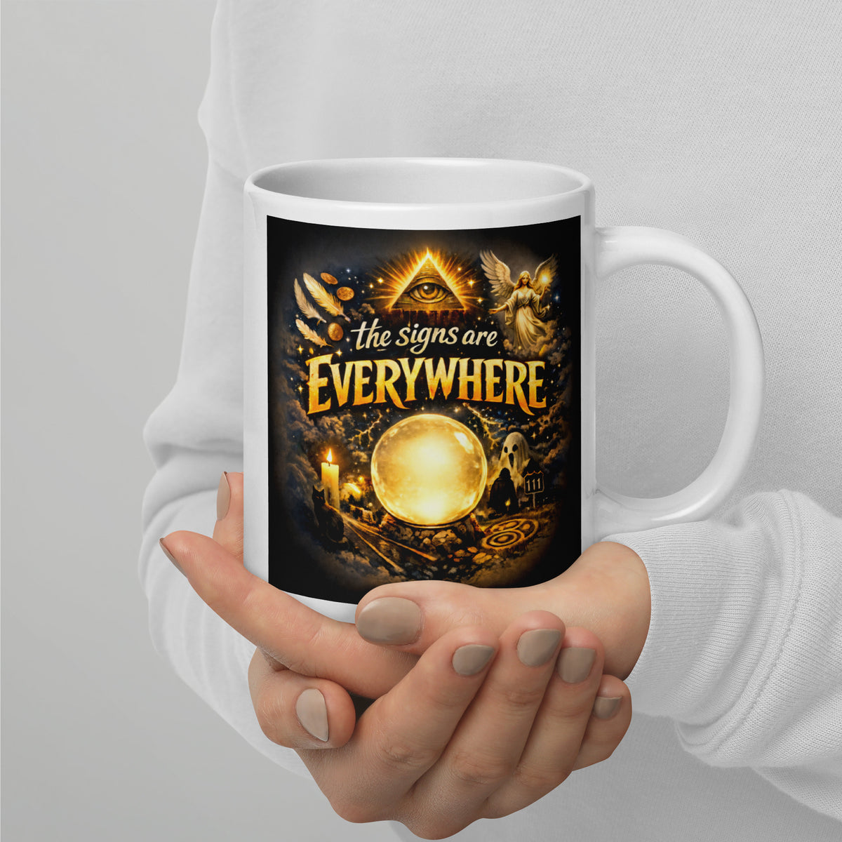 The Signs Are Everywhere design, an all-seeing eye, an angel, a glowing crystal ball, a ghost and a 111 road sign, in gold on black, on a white glossy mug, 20 oz, handle on the right